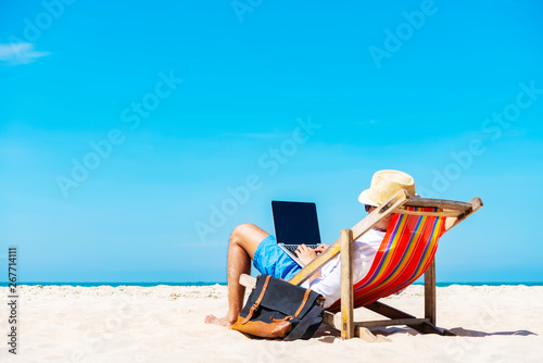 A man using laptop on the tropical beach on vacation. Technology for life concept.