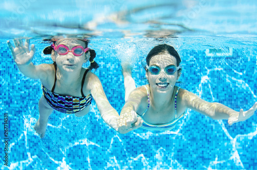 Children swim in swimming pool underwater, happy active girls have fun under water, kids fitness and sport on active family vacation