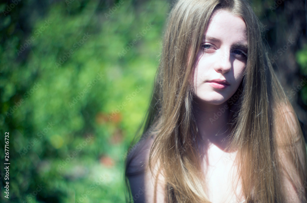 Naklejka premium beautiful young blonde with her long hair against a background of greenery
