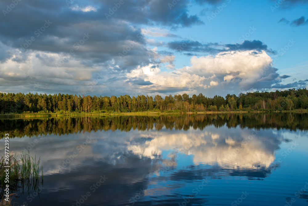 beautiful sunset by the lake with green grass meadow and white clouds in the blue sky beautiful sunset by the lake with green grass meadow and white clouds in the blue sky
