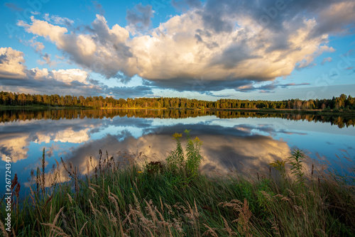 beautiful sunset by the lake with green grass meadow and white clouds in the blue sky