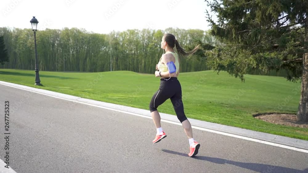 Woman runner run on empty road. Morning time. Slow motion, back view, steady shot Woman runner run on empty road. Morning time. Slow motion, back view, steady shot