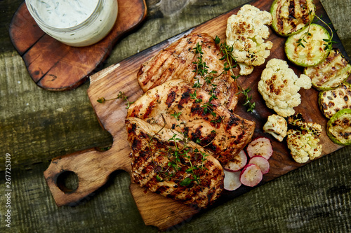 Grilled turkey meat. Steak turkey grill on wooden cutting board with a variety of grilled vegetables on rustic background Top view. Flat lay. Copy space..