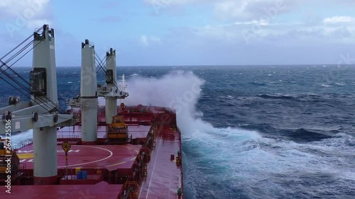 Cargo ship in stormy sea. View from navigation bridge to a large wave crashing into bow of bulk carrier in the stormy sea.
