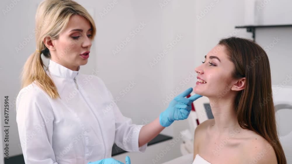 Plastic Surgeon or Cosmetology Specialist Examines Woman's Face, Touches with Hands, Inspecting Healed Skin after Surgery with Amazing Results. Client Sitting on Checkup at Attending Physician Doctor. Plastic Surgeon or Cosmetology Specialist Examines Woman's Face, Touches with Hands, Inspecting Healed Skin after Surgery with Amazing Results. Client Sitting on Checkup at Attending Physician Doctor.