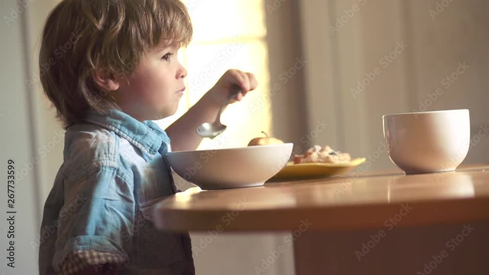 Portrait of beautiful child having breakfast at home. The child in the kitchen at the table eating. Laughing cute child baby boy sitting in highchair and eating on kitchen background. Portrait of beautiful child having breakfast at home. The child in the kitchen at the table eating. Laughing cute child baby boy sitting in highchair and eating on kitchen background.
