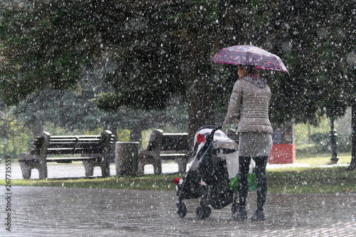 Fényképezés A young mother rolls a stroller with a child in the autumn rain under the umbrel