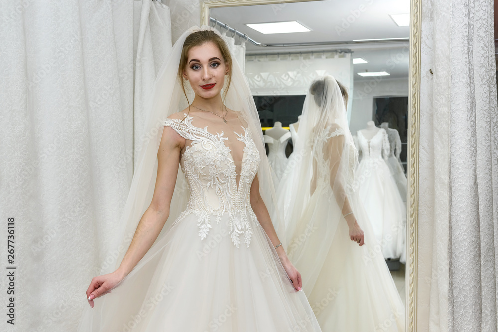 Attractive young woman wearing wedding dress in bridal shop