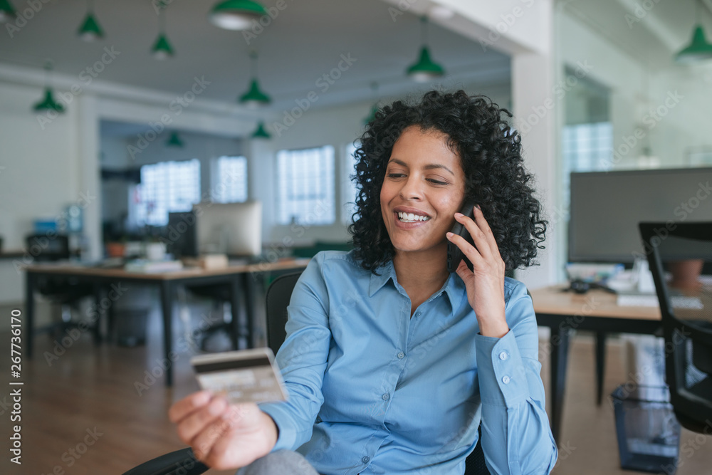 Fototapeta premium Smiling businesswoman ordering something using her cellphone and credit card 