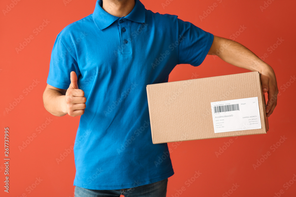 Delivery man with box showing thumb-up on color background Delivery man with box showing thumb-up on color background