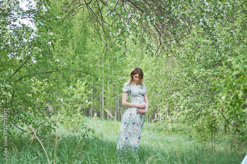 beautiful, pregnant girl in a green dress is standing in a flowered garden