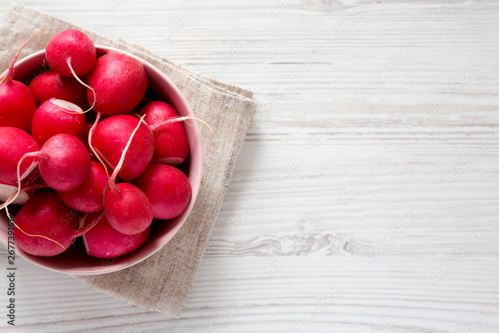 Fresh red radishes in a pink bowl over white wooden background, top view. Flat lay, overhead, from above. Copy space.