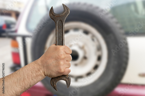 Man showing wrench with car tire in background