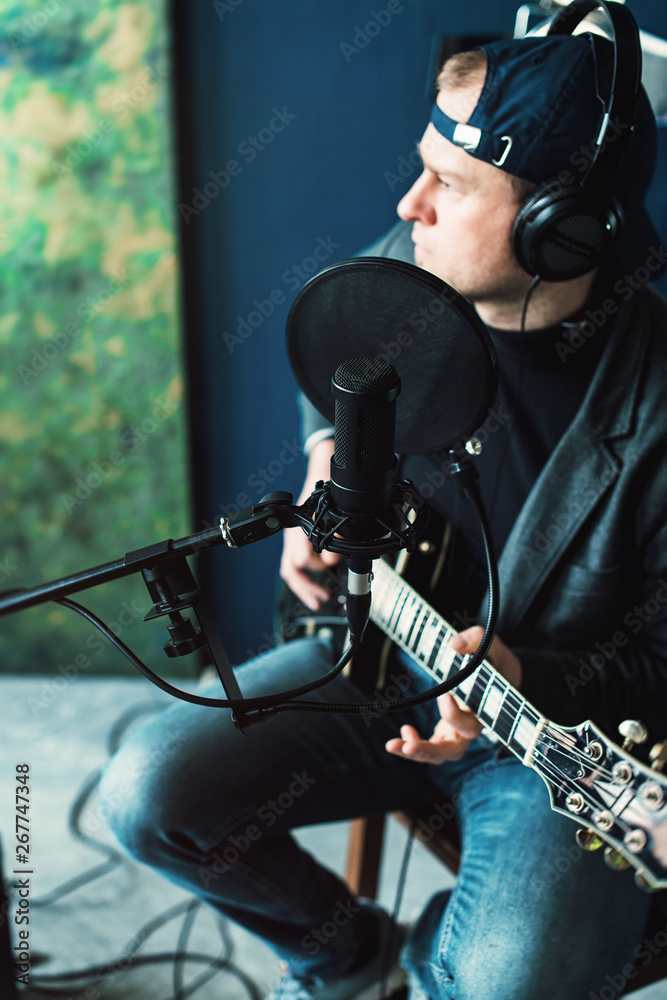 Naklejka premium Close up of a man singer sitting on a stool in a headphones with a guitar recording a track in a home studio