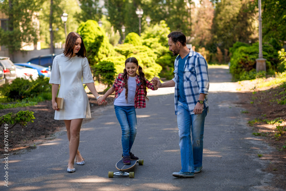 Girl Is Skating In The Park. Mather And Fathert Are Holding Their Daughter.