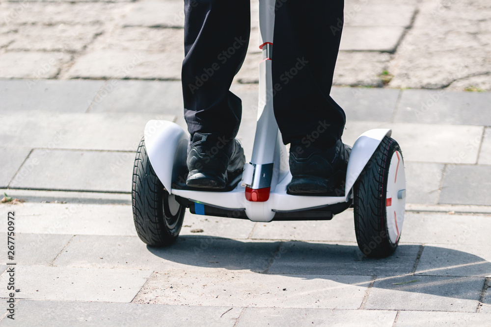 Obraz premium Feet of girl riding electric mini hoverboard scooter on the road. Ecological city transportation on battery power.