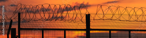 Panorama of a spiny fence on the background of a fiery, bright sunset
