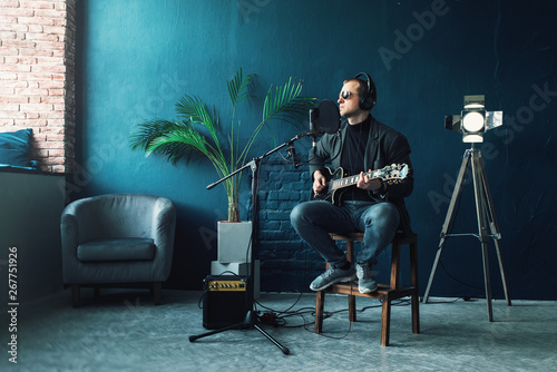 Man singer sitting on a stool in a headphones with a guitar recording a track in a home studio photo