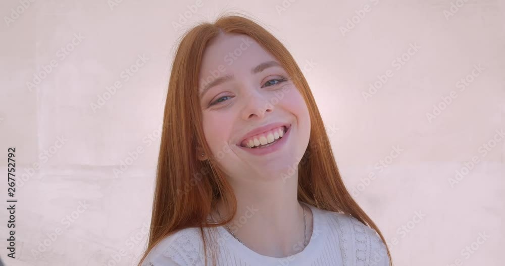 Portrait of pretty ginger model turns to camera and smiles gladly into it on white wall background. Portrait of pretty ginger model turns to camera and smiles gladly into it on white wall background.