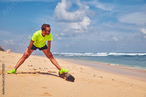 Sportsman stretching on a tropical sandy beach.