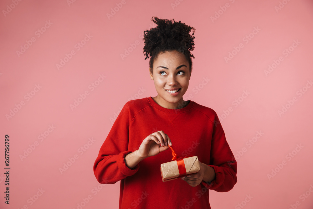 Amazing happy excited young african woman posing isolated over pink wall background holding present box. Amazing happy excited young african woman posing isolated over pink wall background holding present box.
