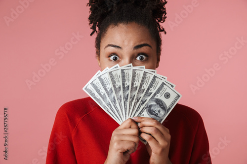 Happy excited young african woman posing isolated over pink wall background holding money.