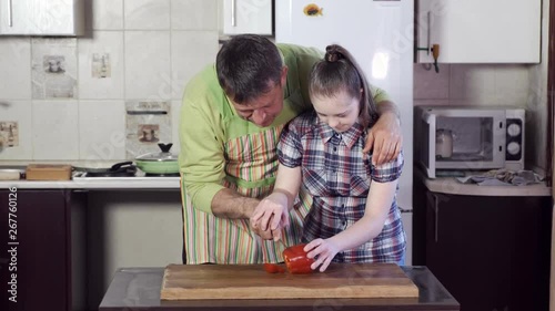 responsible father helps pretty daughter with down syndrome to cut big red bell pepper using knife and cutting board