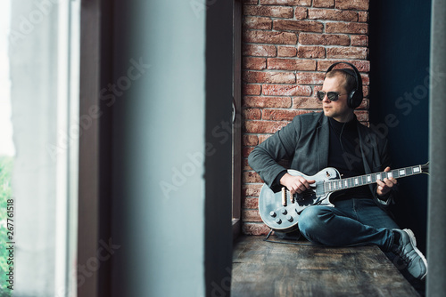 Man singer sitting on a window sill in a headphones with a guitar recording a track in a home studio photo