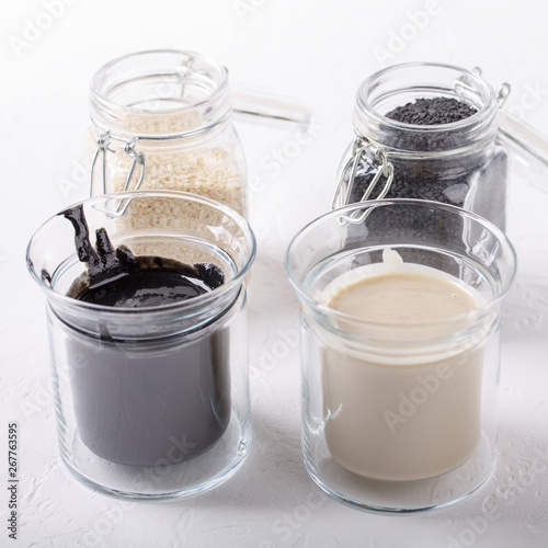 Black tahini and white tahini sauce in glass jars on white background. Natural paste made from sesame seeds. photo