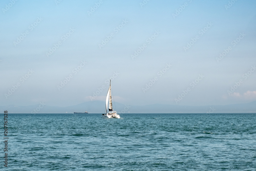 Luxury yacht with white sails in open sea at beautiful sunny day. Small waves on the sea and white clouds on horizon line. Weekend getaway from city. Wonderful world. Natural background. 