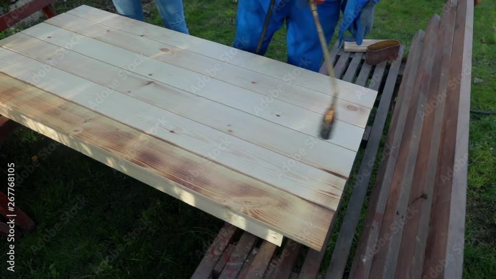A happy young family varnishes a table made of natural material on its own. Refusal of plastic. The table is stelan of planks, made by firing texture.
