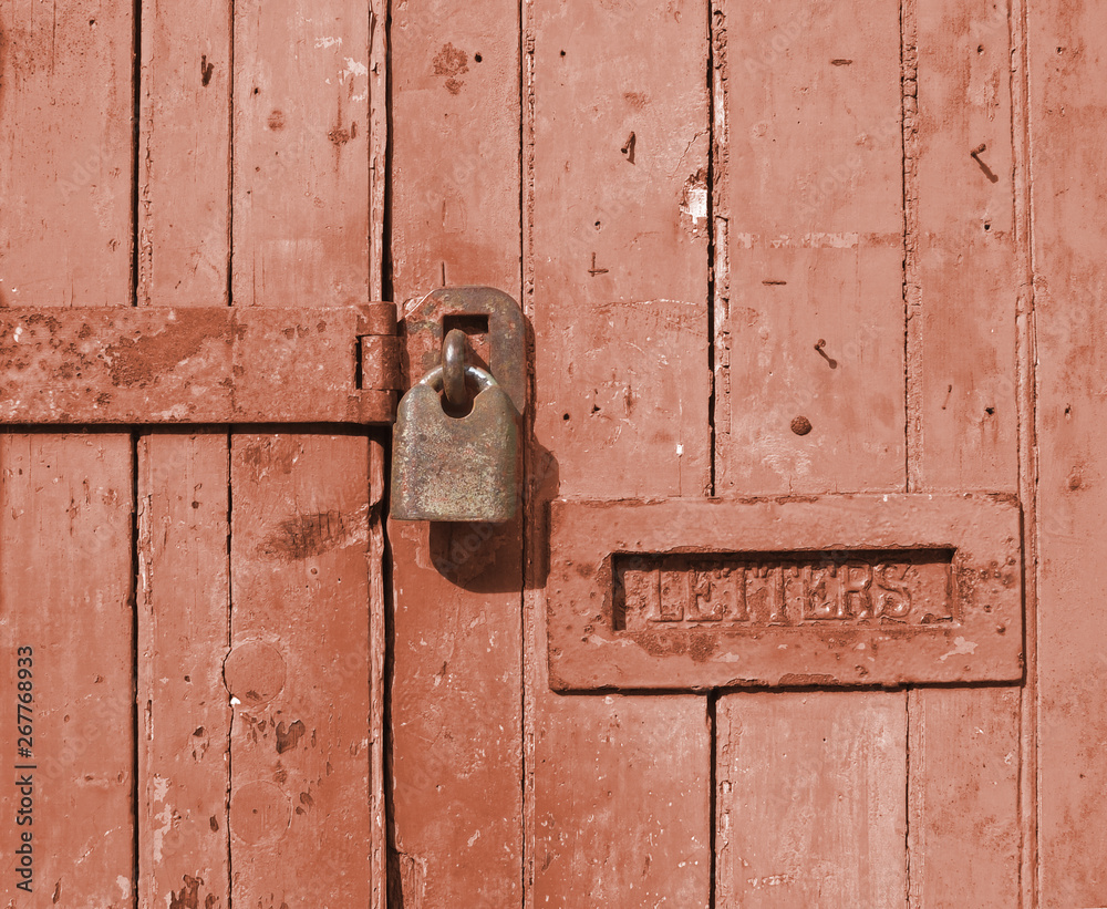 close up of an old brown wooden door with faded paint and a rusty closed padlock and old metal letterbox