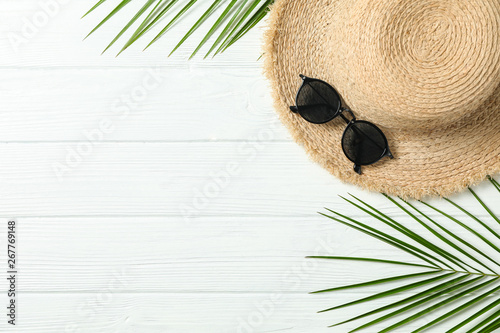 Straw hat, sunglasses and palm leaves on white wooden background, space for text and top view. Summer vacation backdrop #267769148