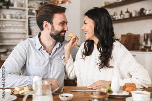 Portrait of attractive brunette couple eating together at table while having breakfast in kitchen at home