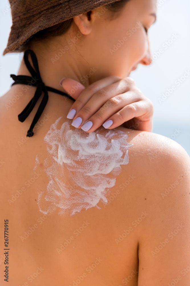 © sosiukin - Beautiful woman in hat is putting sun cream on her shoulder at the beach © sosiukin - Beautiful woman in hat is putting sun cream on her shoulder at the beach