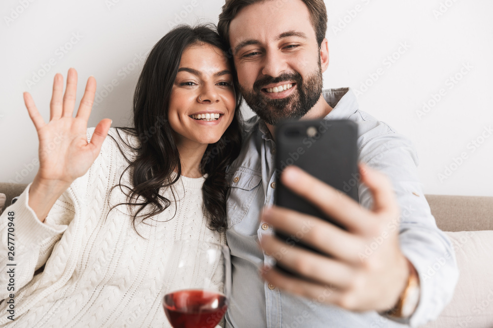 Image of caucasian couple taking selfie photo together on sofa while drinking wine in bright room Image of caucasian couple taking selfie photo together on sofa while drinking wine in bright room