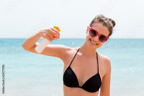 Young woman is holding a bottle of sunblock for body at the sea background