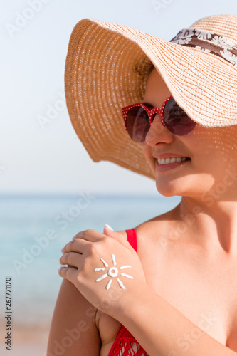 Young woman with sun shape on her hand made of sunscreen at the beach