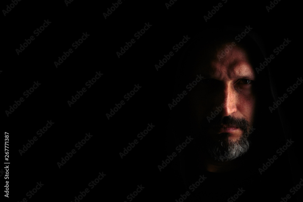 Brutal man with a gray beard in the hood with sharp shadows on a black background. Copy space. Brutal man with a gray beard in the hood with sharp shadows on a black background. Copy space.