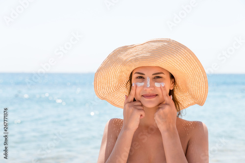 Bilde på lerret Pretty woman protects her skin on face with sunblock at the beach