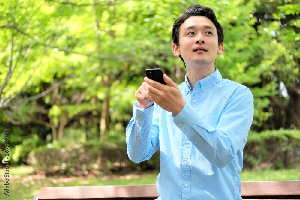 公園でスマホ　携帯を操作する三十代男性