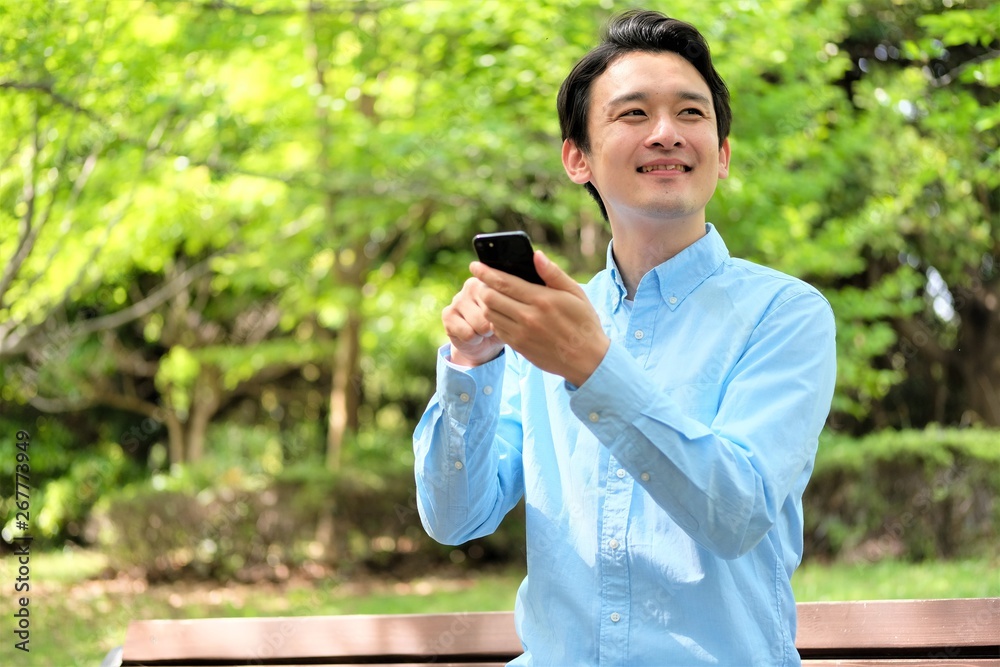 公園でスマホ 携帯を操作する三十代男性 公園でスマホ 携帯を操作する三十代男性