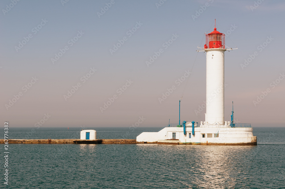 Beautiful big white red lighthouse against the calm sea, cloudless sky and clear horizon - a symbol of the safe path for ships, vintage tone. Beacon on the edge of the pier. Seascape of Black sea.