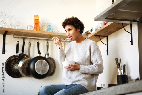 young african americna woman eating cereal in kitchen at home photo