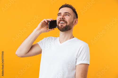 Happy man posing isolated over yellow wall background talking by phone.