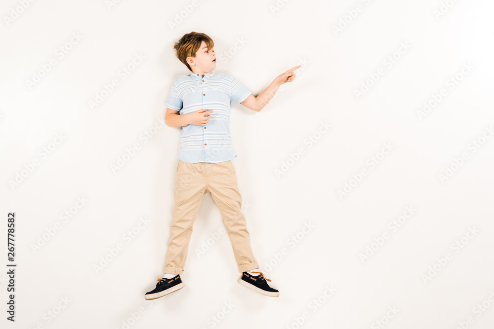 top view of surprised kid pointing with finger while lying on white top view of surprised kid pointing with finger while lying on white