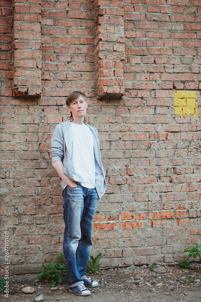 young 30s age man in white and blue casual clothing standing with his hands in pockets in full size near old red brick wall background, urban lifestyle stock photo image young 30s age man in white and blue casual clothing standing with his hands in pockets in full size near old red brick wall background, urban lifestyle stock photo image