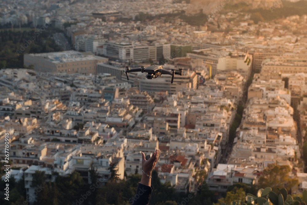 Man's hand catching drone with city landscape. Beautiful view on sunset.