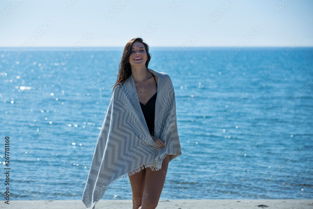 Pretty young girl wrapped in beach towel poses to camera. Full length photo shoot and wonderful hair. Healthy, beauty and summer holiday concept. Pretty young girl wrapped in beach towel poses to camera. Full length photo shoot and wonderful hair. Healthy, beauty and summer holiday concept.