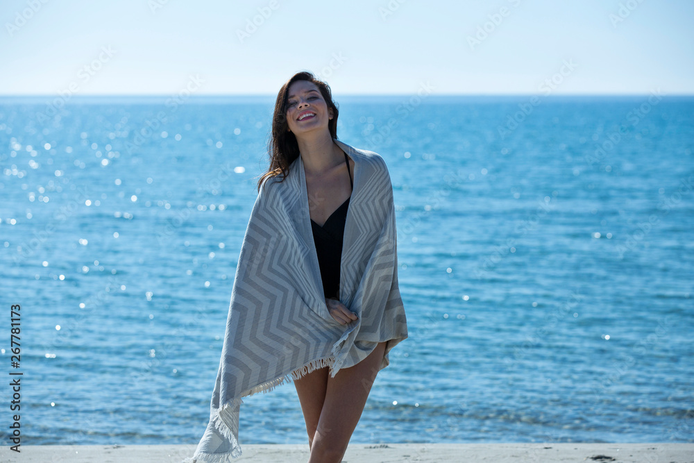 Pretty young girl wrapped in beach towel poses to camera. Full length photo shoot and wonderful hair. Healthy, beauty and summer holiday concept. Pretty young girl wrapped in beach towel poses to camera. Full length photo shoot and wonderful hair. Healthy, beauty and summer holiday concept.